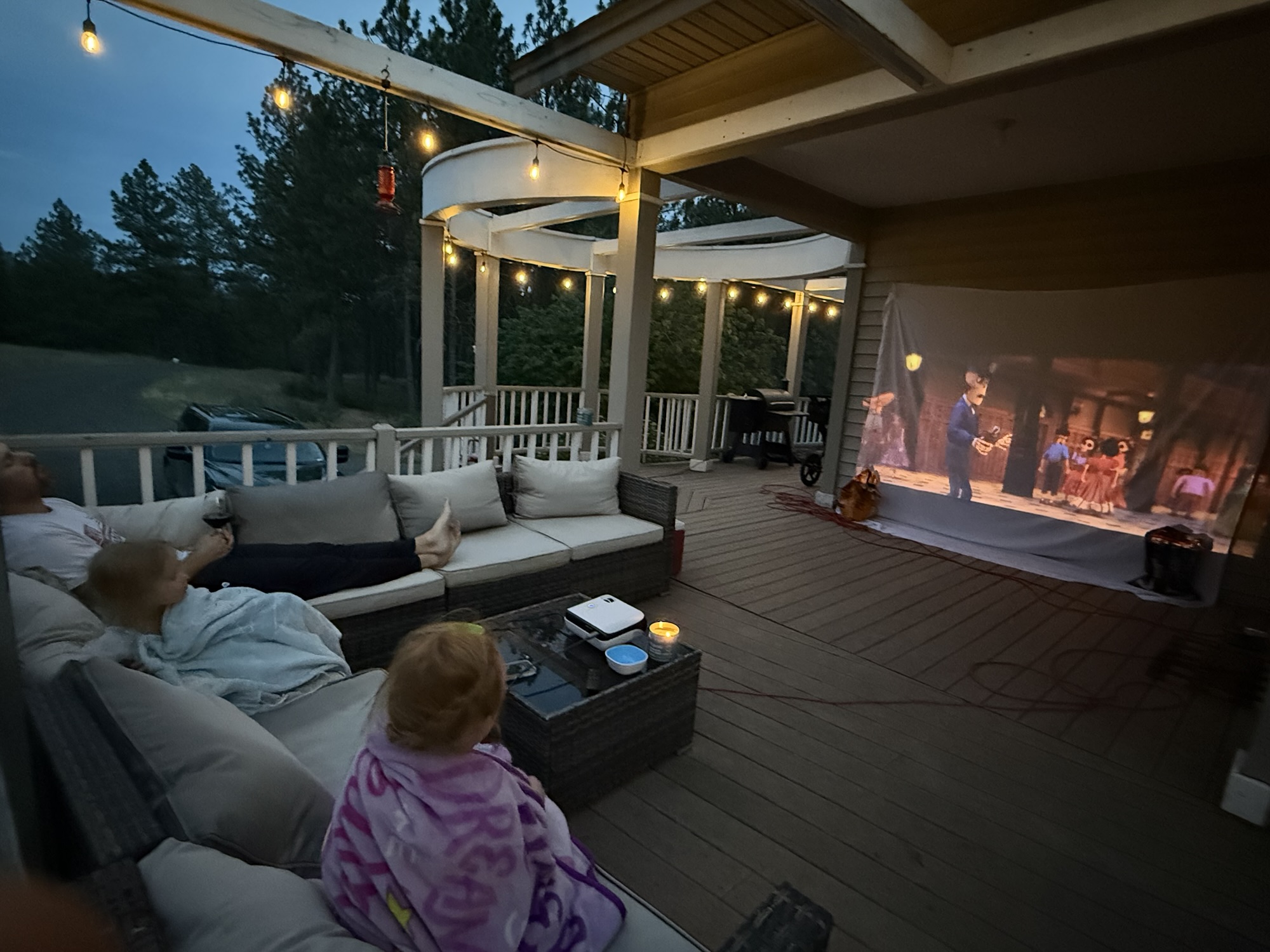 Backyard patio set up for an outdoor family movie night with cozy seating, a fire pit and a white sheet for a projector screen.