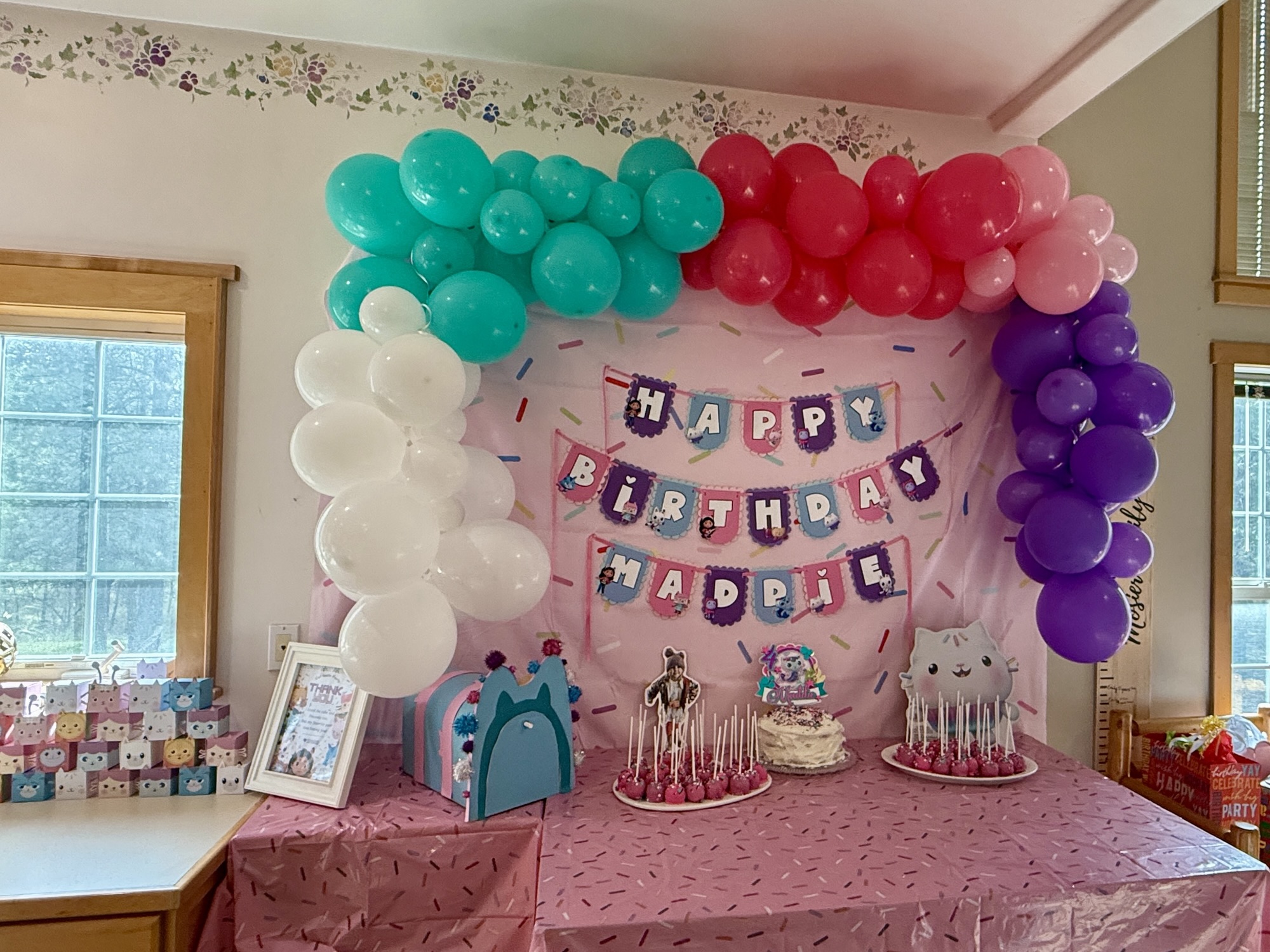 Colorful Gabby's Dollhouse birthday party setup with balloon garlands, themed decorations, and party favors.