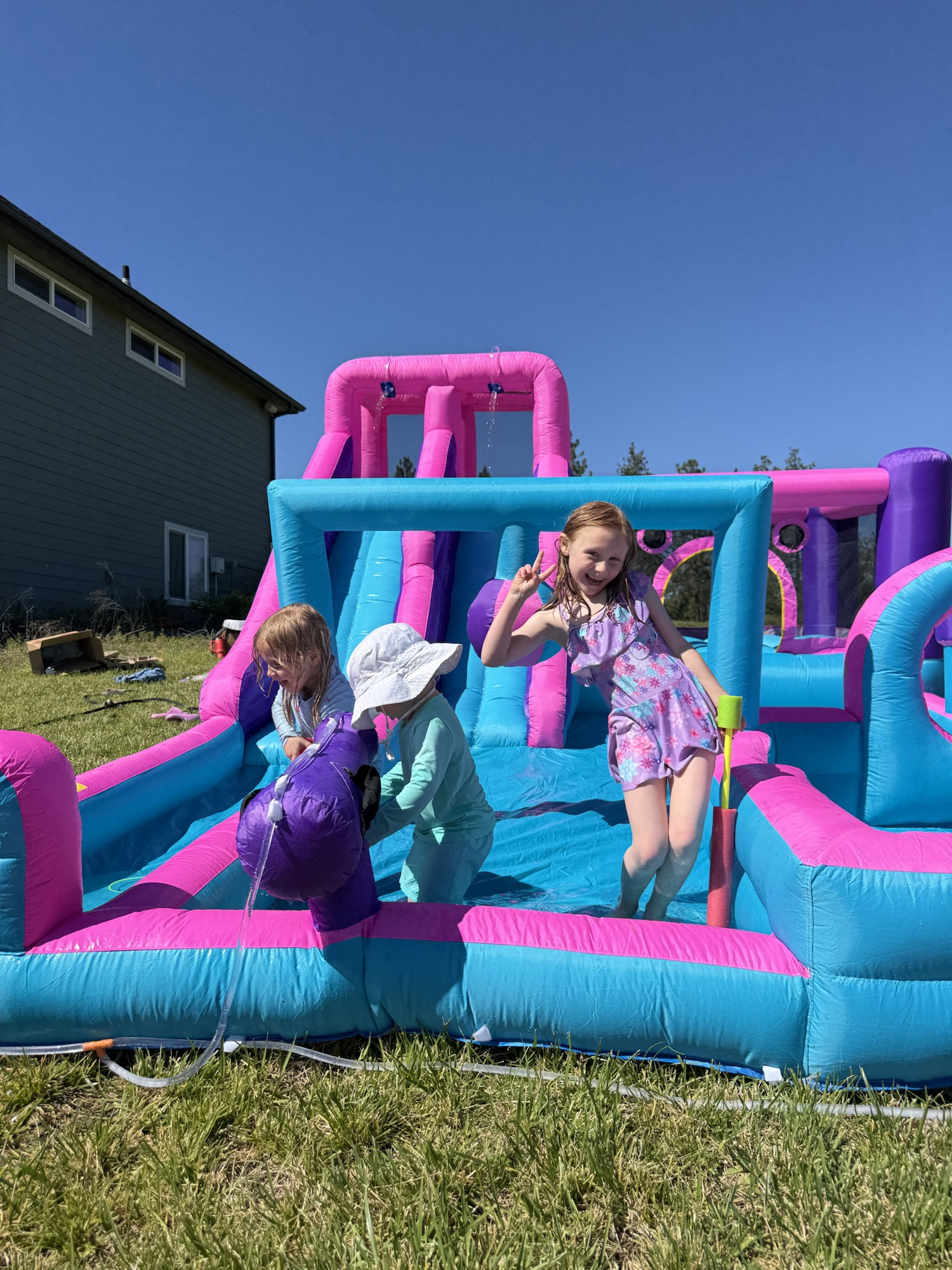 Kids playing on a colorful inflatable bounce house with slide during a sunny day.