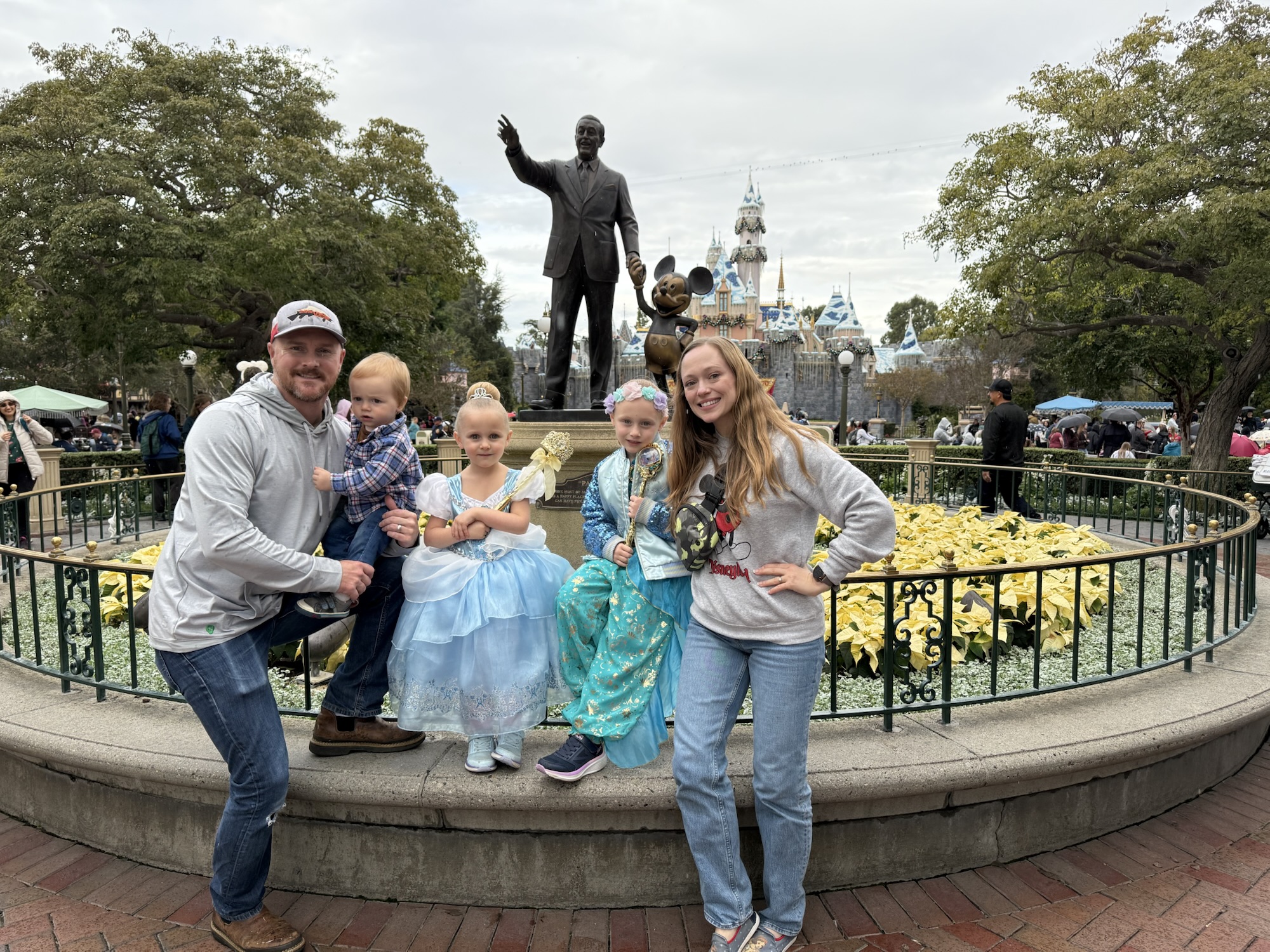 Family posing together at Disneyland with Sleeping Beauty Castle in the background.