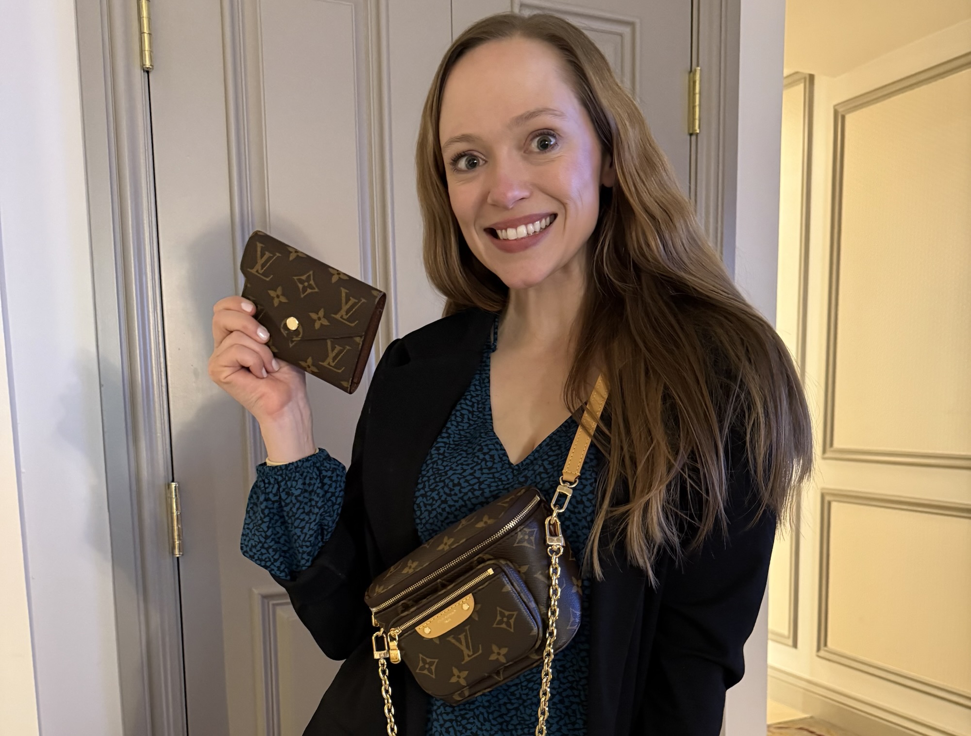 A woman wearing her new Louis Vuitton Mini Bumbag crossbody and holding a matching Louis Vuitton monogram wallet.